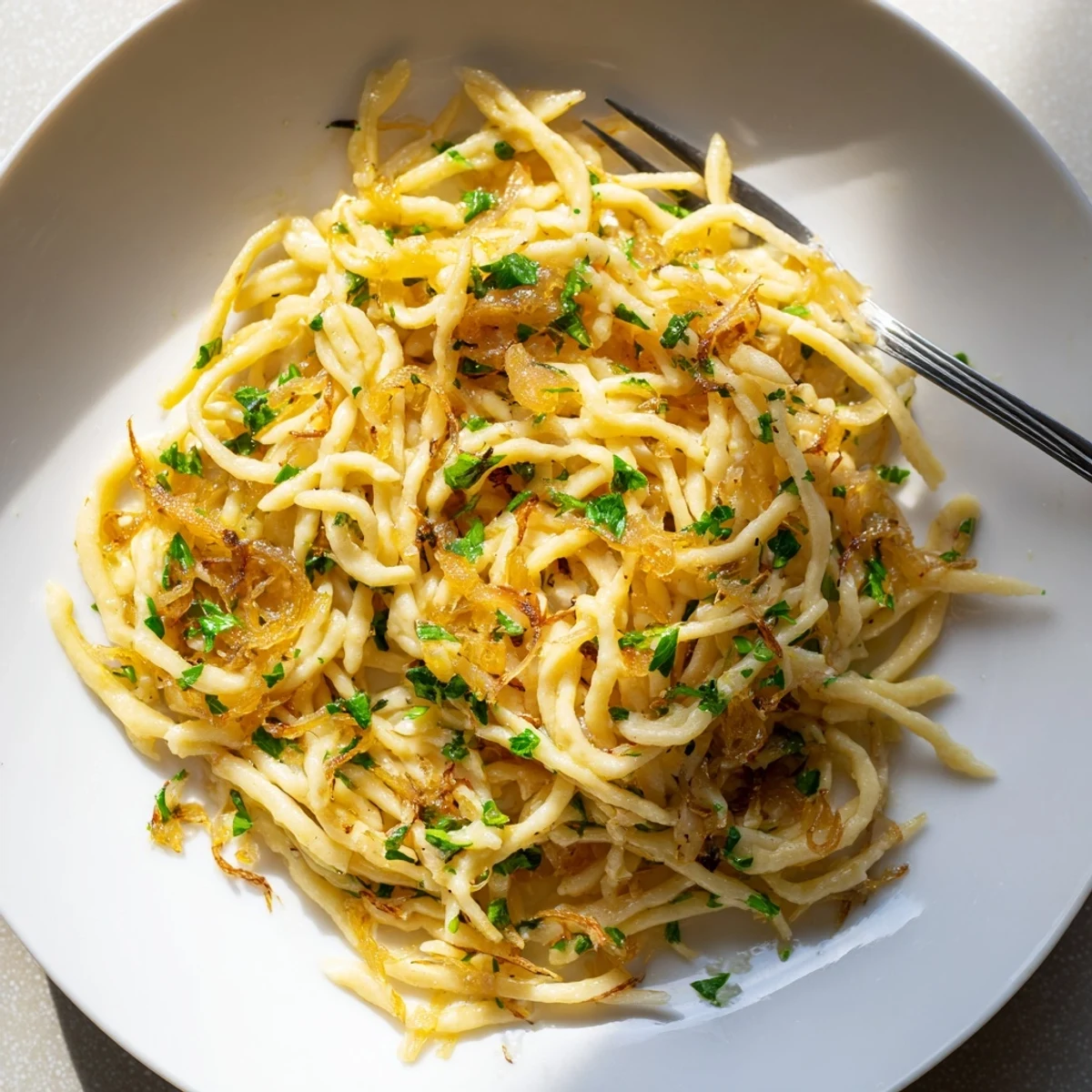 Zarte deutsche Spaetzle mit süß-karamellisierten Zwiebeln und frischen Kräutern.