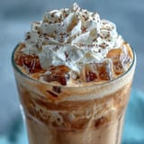 Vanille-Bohnen-Frappuccino-Kopie mit Cold Brew-Eiswürfeln in einem hohen Glas, mit geschlagener Sahne und Vanille-Garnitur garniert.