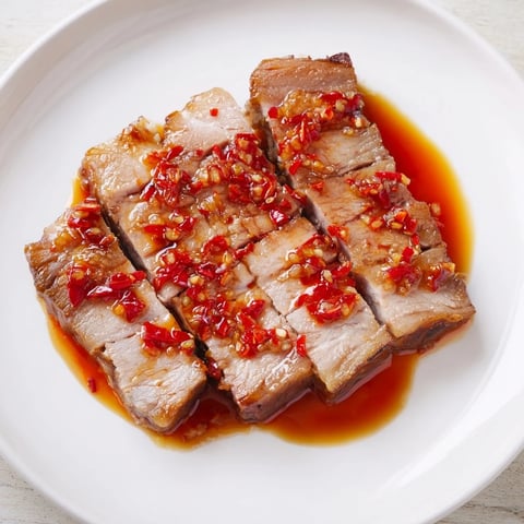 Juicy Bavarian roast pork with crispy skin, drizzled with spicy chili-ginger sauce for dinner.