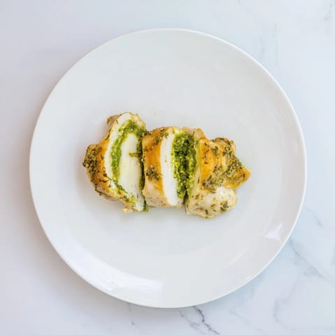 Golden-baked Mozzarella & Pesto Stuffed Chicken breasts served with a fresh green salad on a plate.