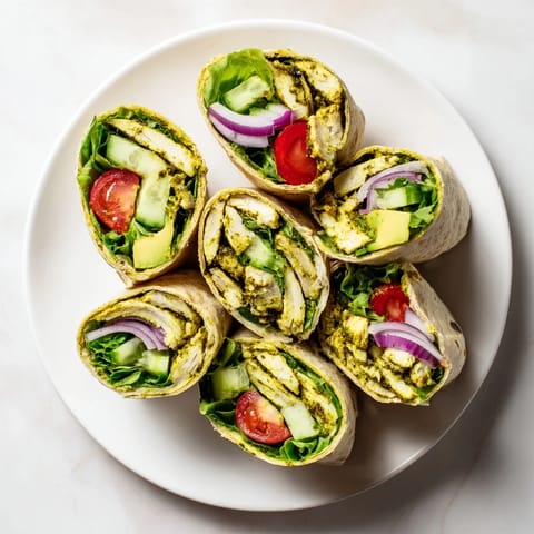 Ein Chimichurri Chicken Salad Wrap liegt auf einem Holztisch, umgeben von frischen Kräutern und einer Zitrone.