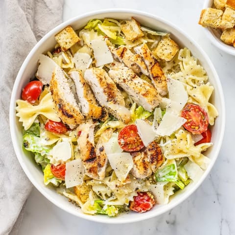 Grilled chicken slices and crisp romaine on penne pasta with creamy Caesar dressing, served in a vibrant bowl.