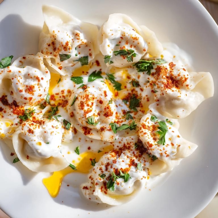 A close-up of savory Turkish cheesy manti, perfectly cooked and arranged on a plate with sauce.