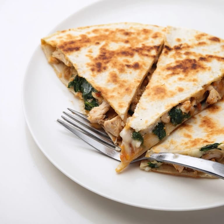 Freshly grilled Chicken and Spinach Quesadilla triangles arranged neatly beside a bowl of creamy salsa dip.