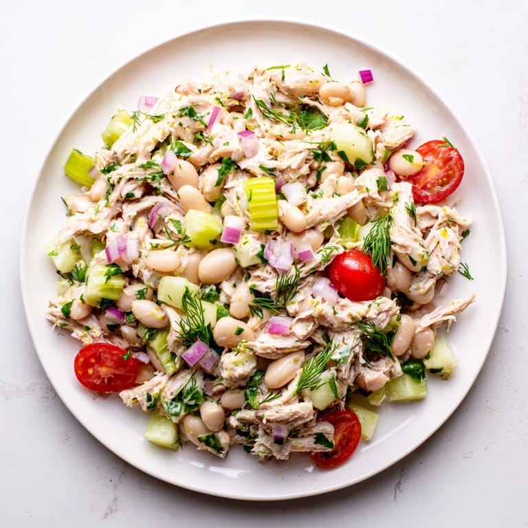 Eine oberansicht des Lemony White Bean Chicken Salads mit saftigem Hähnchen und halbierten Kirschtomaten auf rustikalem Holz.